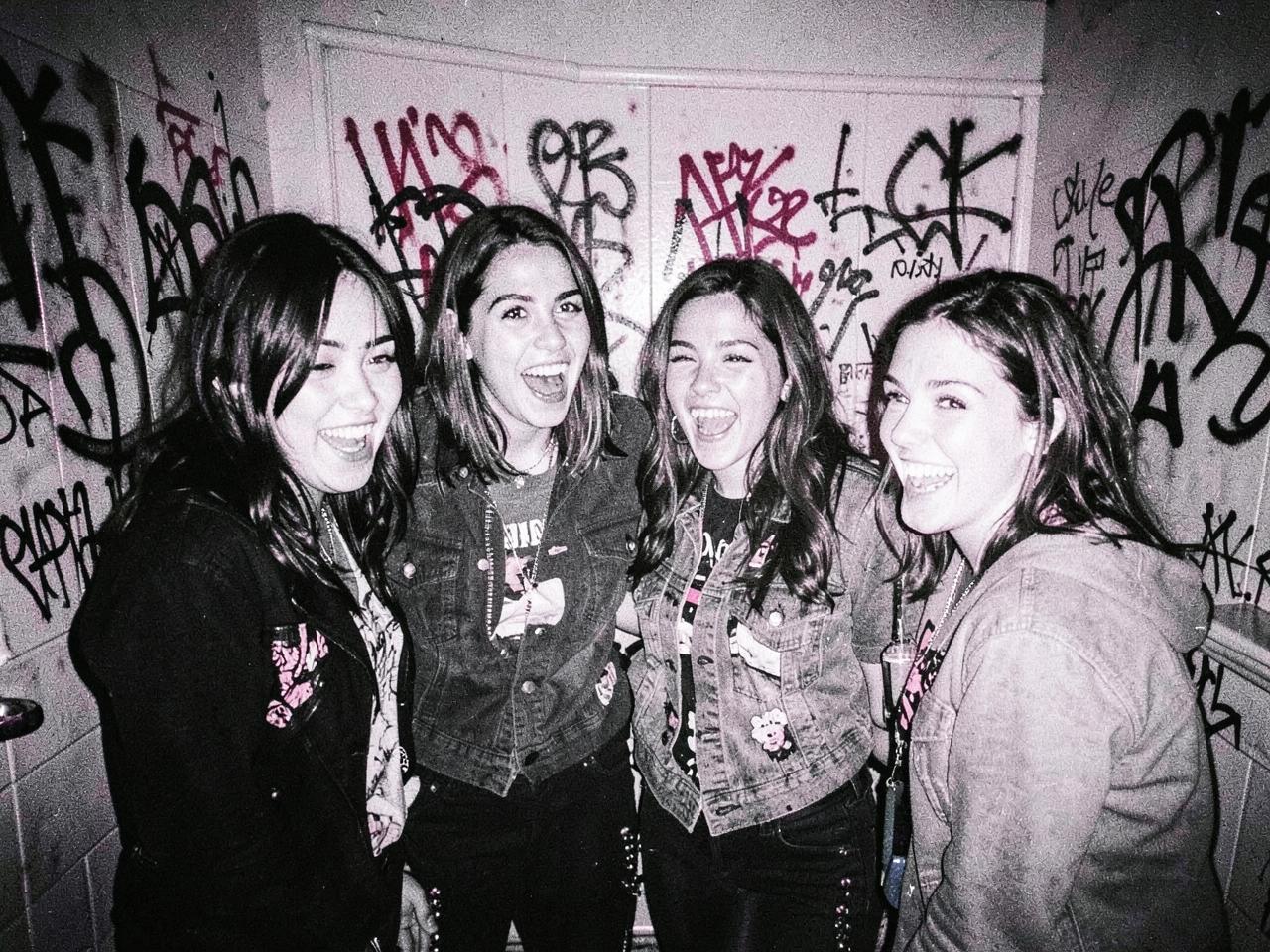Four friends laughing in a graffiti-covered bathroom, shot on flash